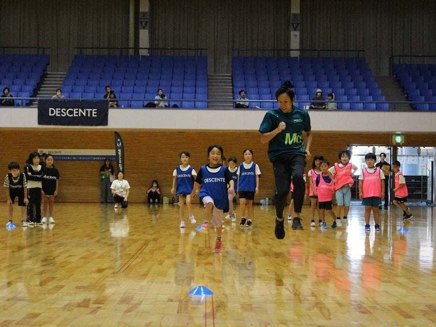 Children running a drill in a gym alongside an athlete